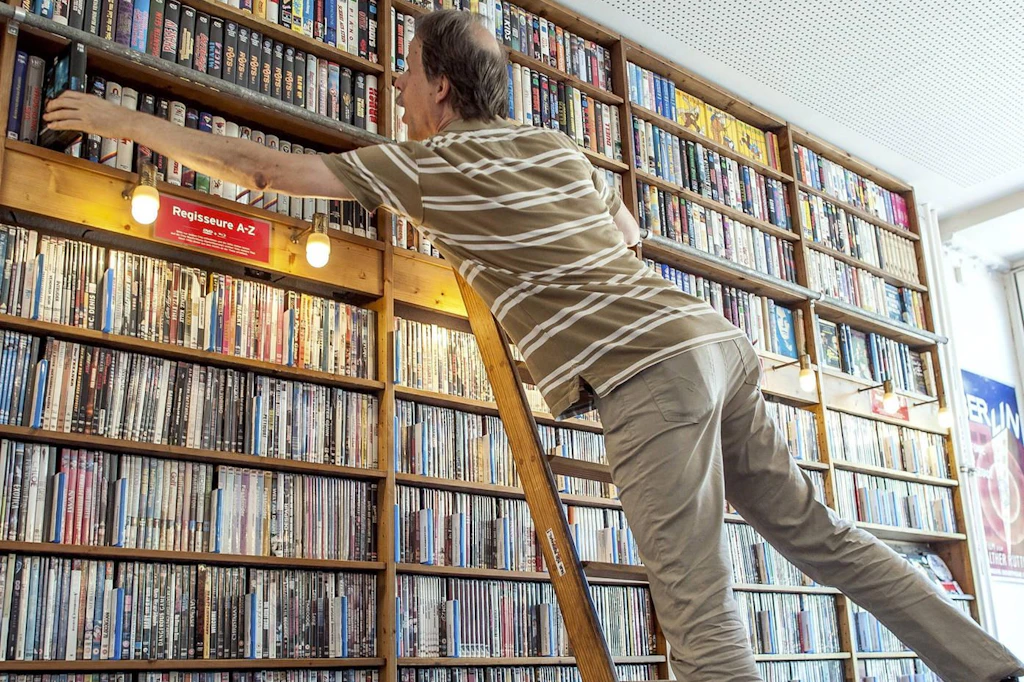 Ein Mann auf einer Leiter vor einem Regal mit DVDs.