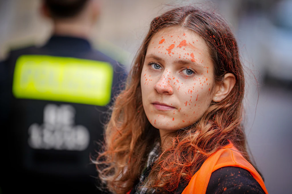 Lina Schinköthe, Klimaaktivistin der Organisation „Letzte Generation“ steht vor der Parteizentrale der FDP zwischen Polizeibeamten. Zuvor wurde die Parteizentrale mit Farbe besprüht.