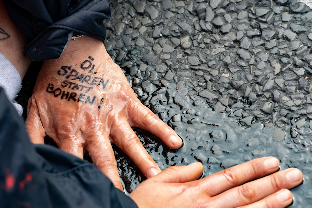 „Öl sparen statt bohren“ steht auf der Hand einer Demonstrantin der Gruppe „Letzte Generation“, die sich auf dem Asphalt festgeklebt hat.
