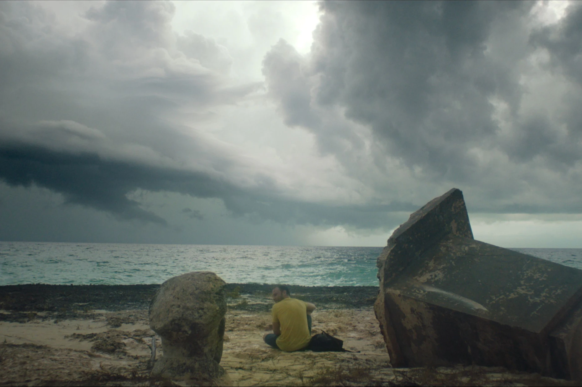 Dunkle Wolken ziehen am Horizont auf. Am Strand ist der Kopf der Ernst Hermann Wüste zu sehen. Das Denkmal wurde bereits in den 90er-Jahren durch einen Hurrikan zerstört. Dieses Bild von der DDR-Insel ist in dem Spielfilm „Ernesto’s Island“ (2023) zu sehen.