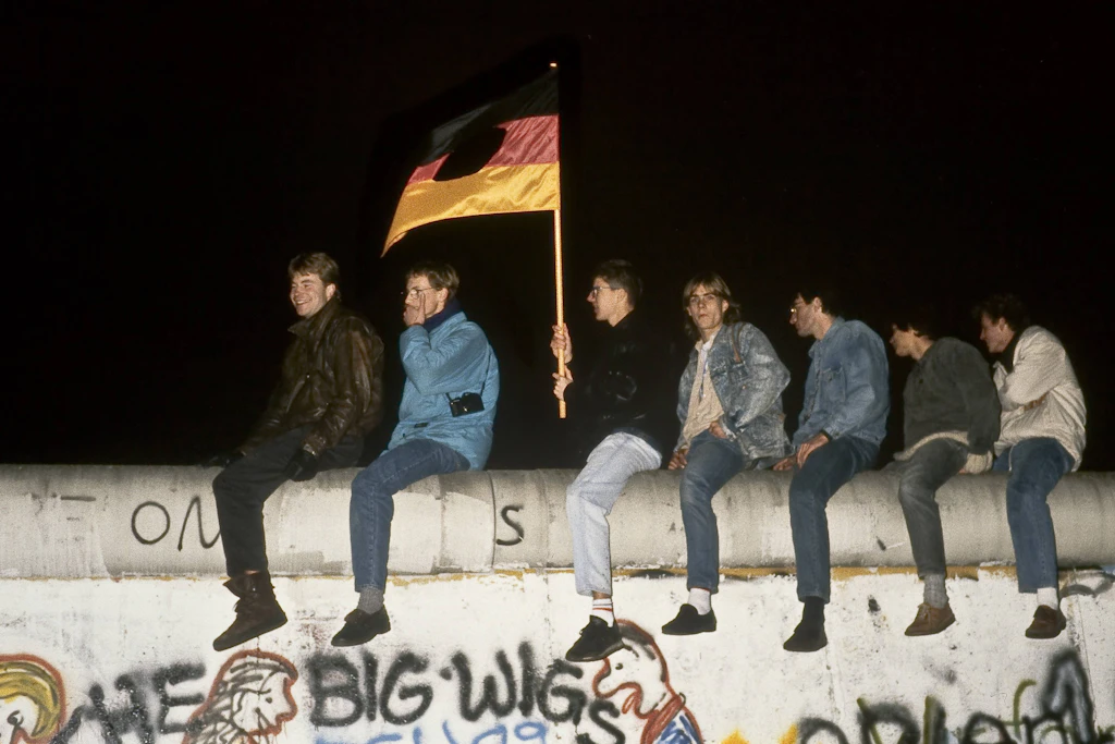 Berliner feiern auf der Berliner Mauer, das Emblem aus der DDR-Fahne haben sie ausgeschnitten.