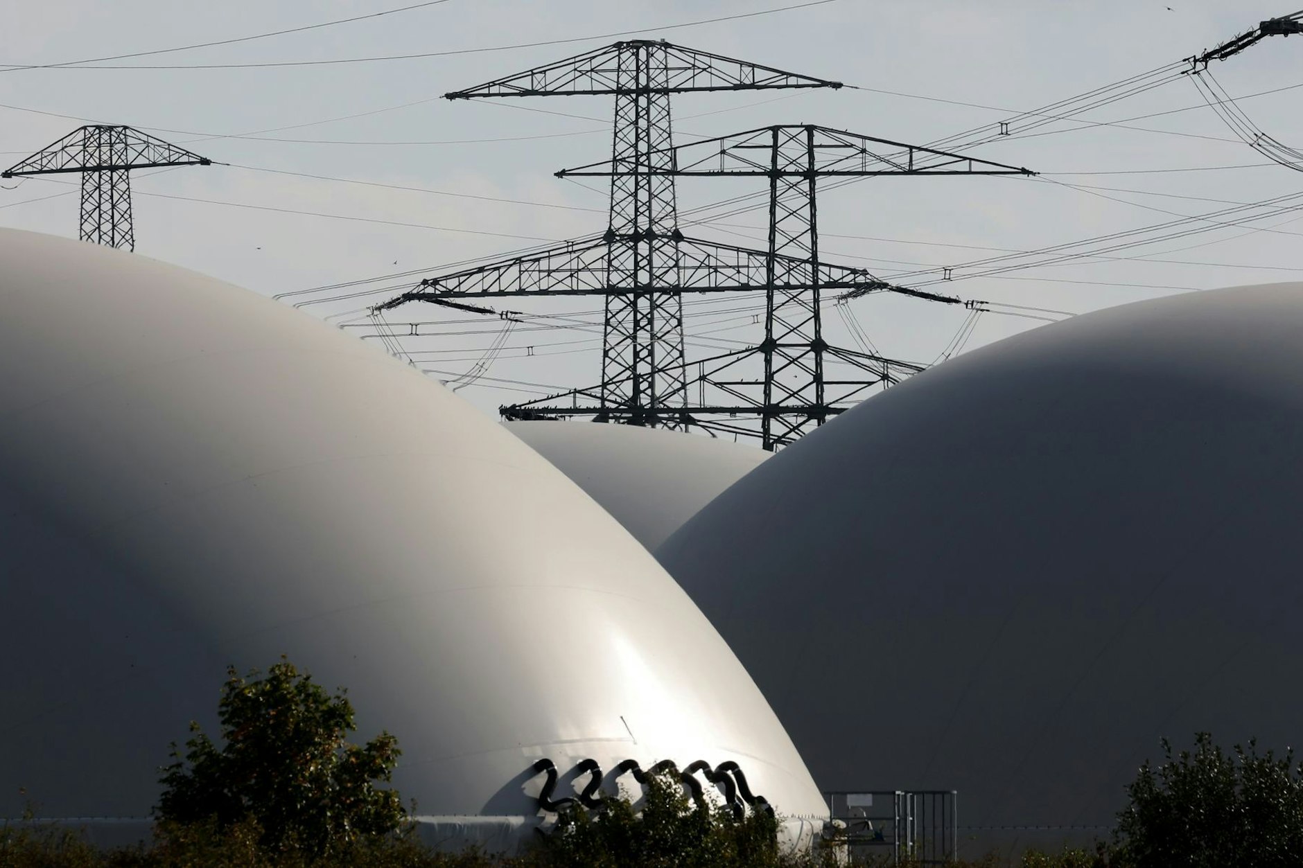 Hochspannungsmasten hinter den Speichern einer Biogasanlage: Wird die Industrie so in Zukunft mit einem Mix aus Erd- und Biogas versorgt?