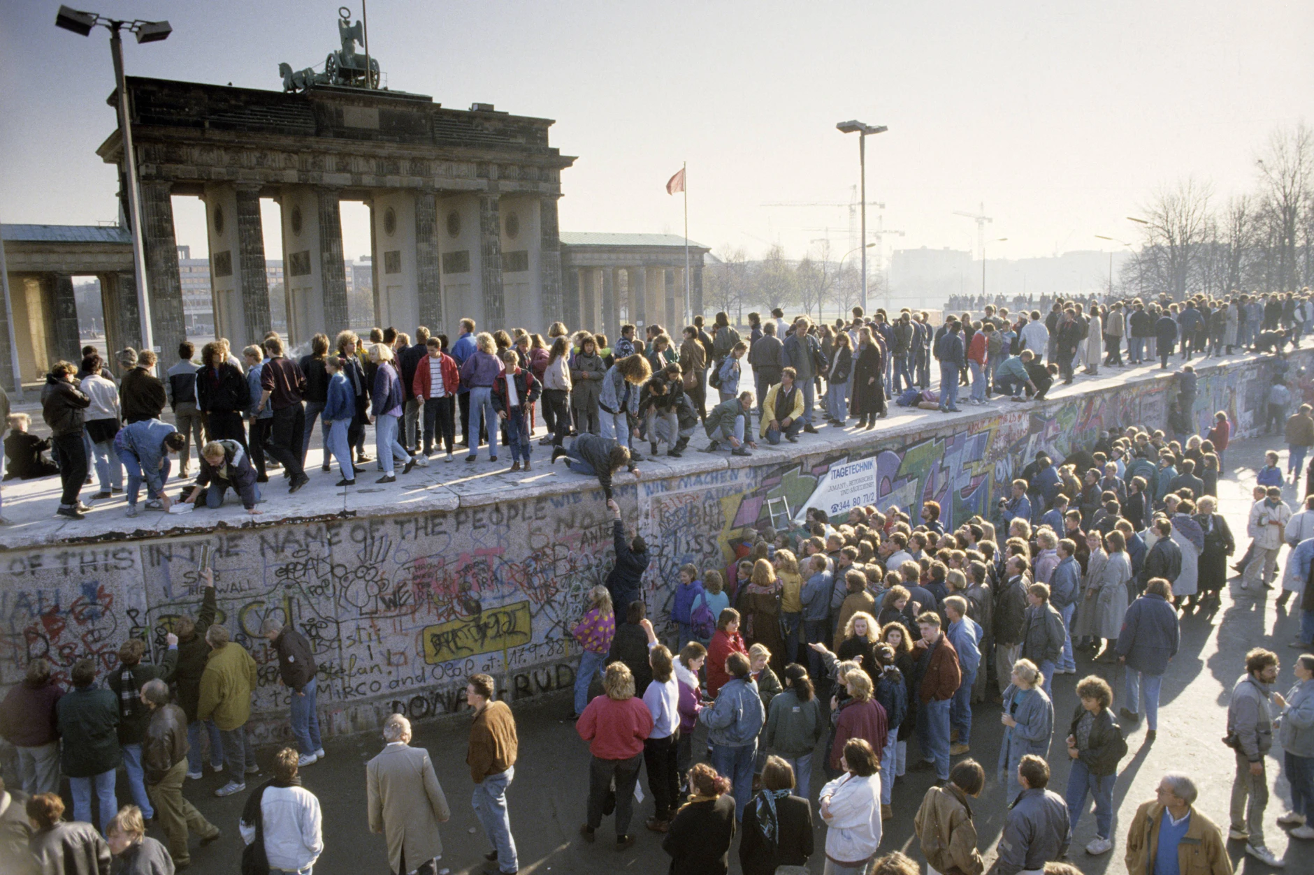 Menschenmassen auf und vor der Berliner Mauer am Brandenburger Tor während des Mauerfalls.