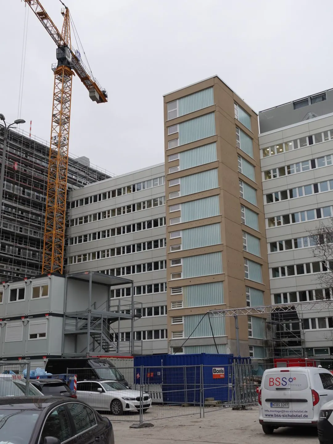 Auf der Rückseite: Das Licht brennt schon, Fassaden, Fenster und Treppenhäuser des Querriegels sind fertig.