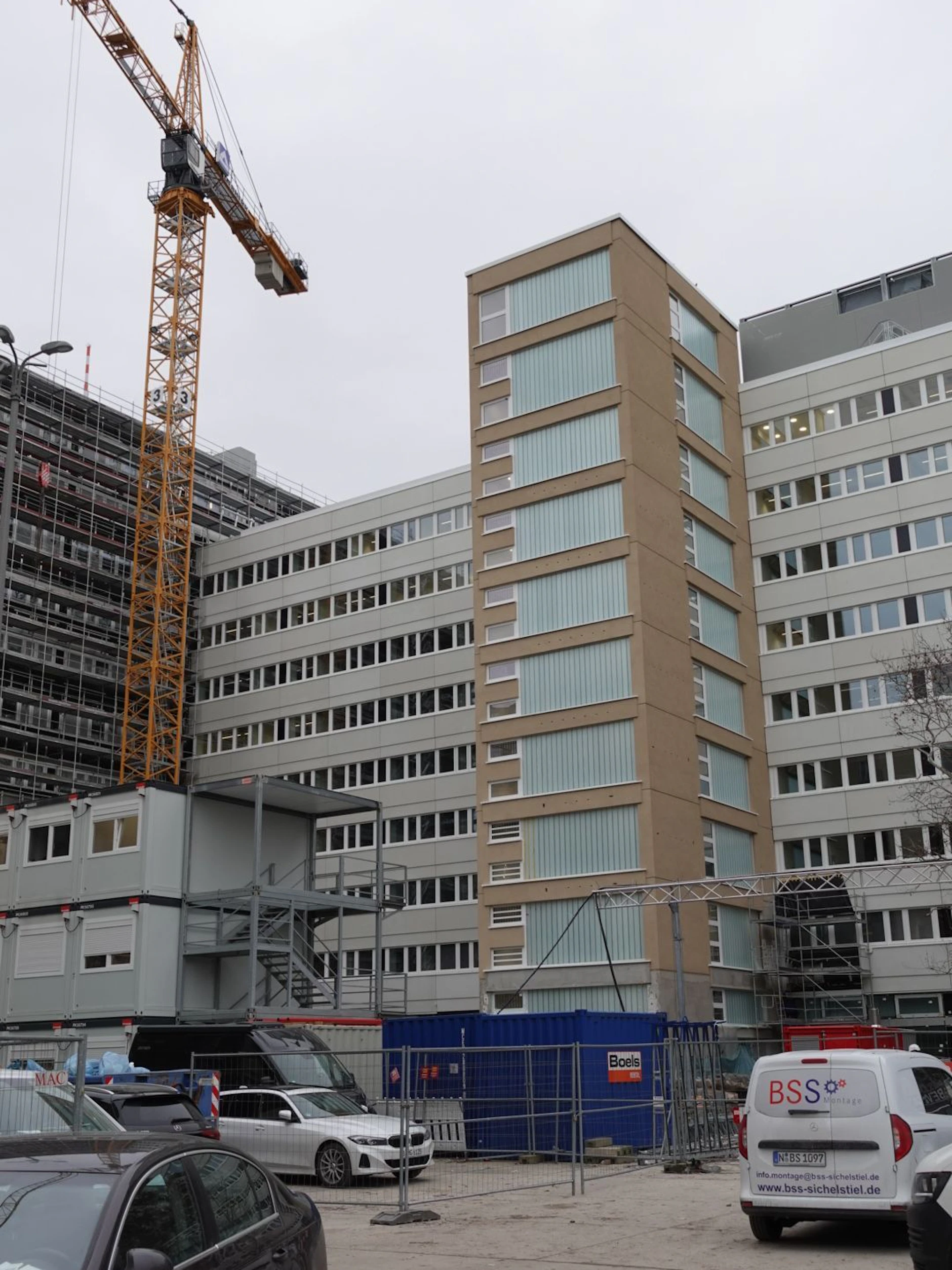 Auf der Rückseite: Das Licht brennt schon, Fassaden, Fenster und Treppenhäuser des Querriegels sind fertig.