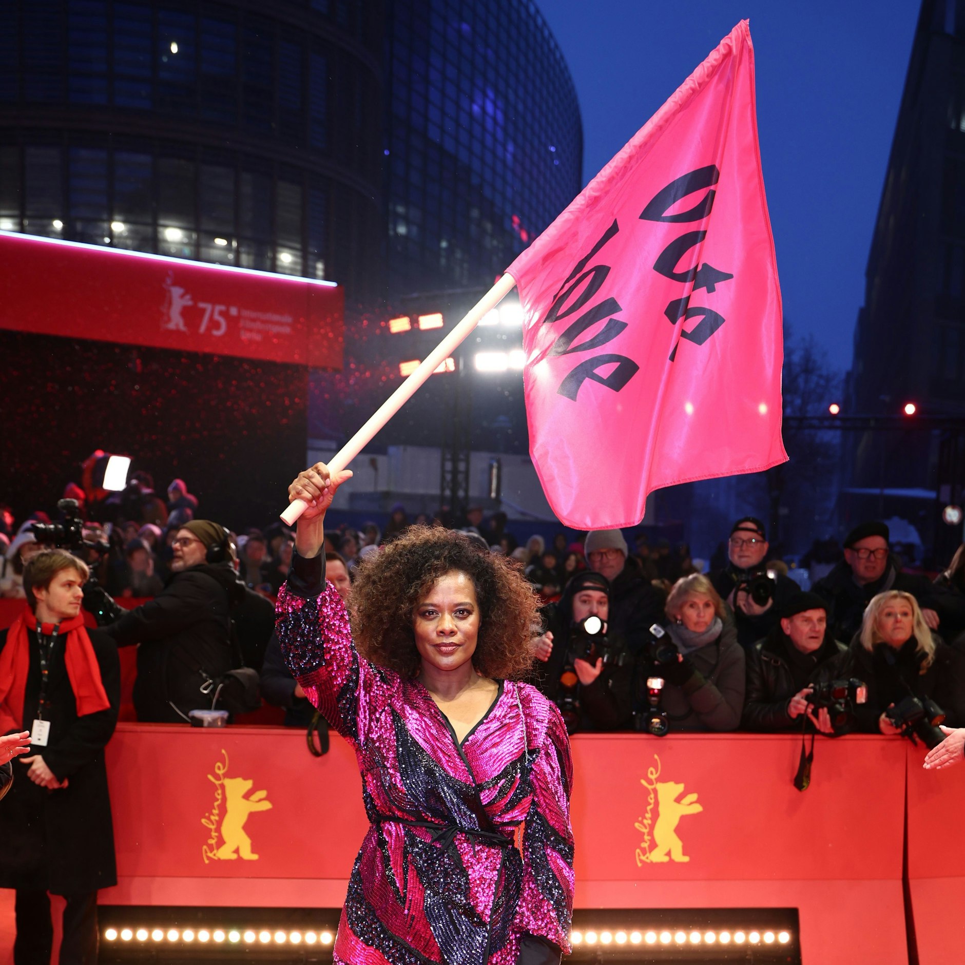 Schauspielerin Denise M'Baye steht mit einer Flagge mit der Aufschrift "vote love" am Eröffnungsabend der Berlinale auf dem Roten Teppich.