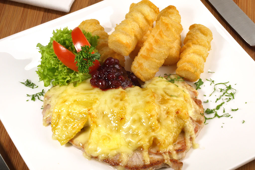 Steak Hawaii: Die Schweinesteaks werden mit Ananas belegt und mit Käse überbacken. Dazu passen Kroketten.