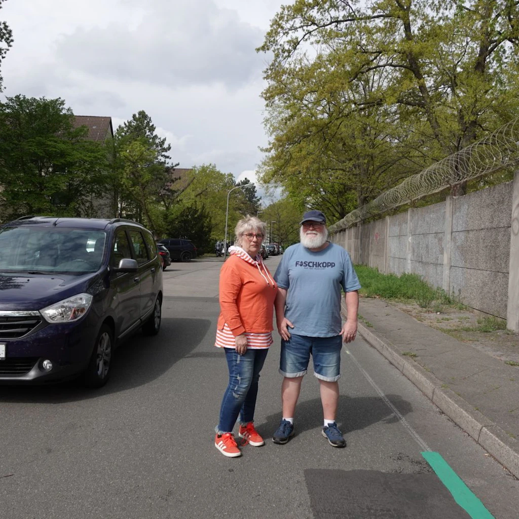 Christine Holm und Michael Wilke, beide Anwohner und Kleingärtner, stehen dort, wo die Straße geteilt wird: Das Ende des grünen Streifens zeigt das Ende der Fahrradstraße, dahinter werden Autos ganz normal fahren und parken dürfen.