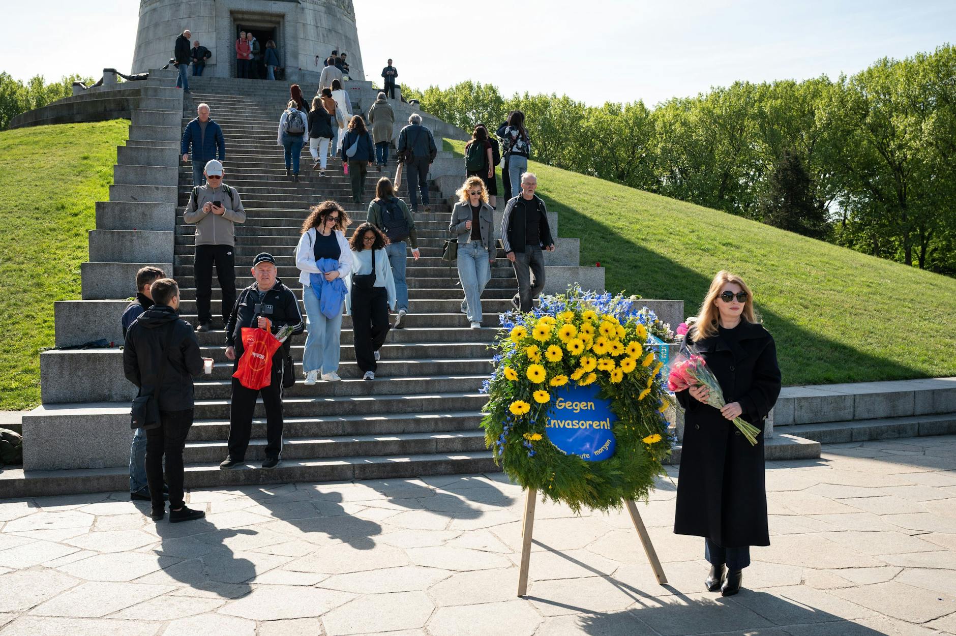 Sowjetisches Ehrenmal in Treptow: Eine Frau mit Blumenstrauß posiert vor einem Kranz, welcher an die aktuelle Invasion Russlands in die Ukraine erinnert.