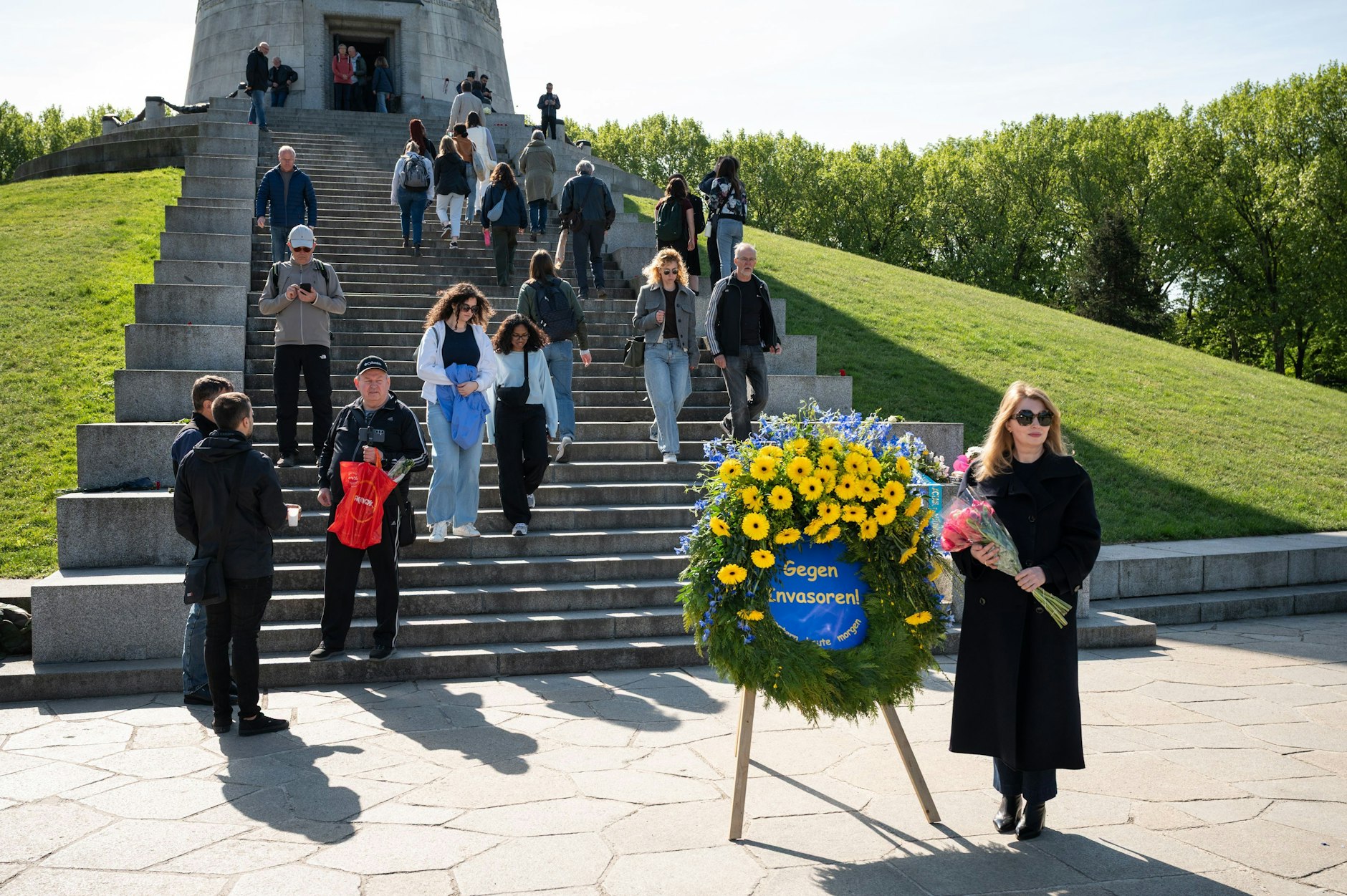 Sowjetisches Ehrenmal in Treptow: Eine Frau mit Blumenstrauß posiert vor einem Kranz, welcher an die aktuelle Invasion Russlands in die Ukraine erinnert.