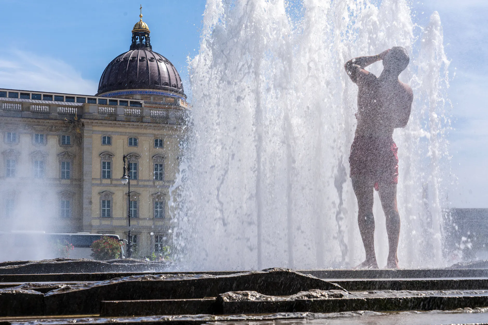 Ein Mann findet Abkühlung unter der Fontäne vor dem Berliner Stadtschloss.