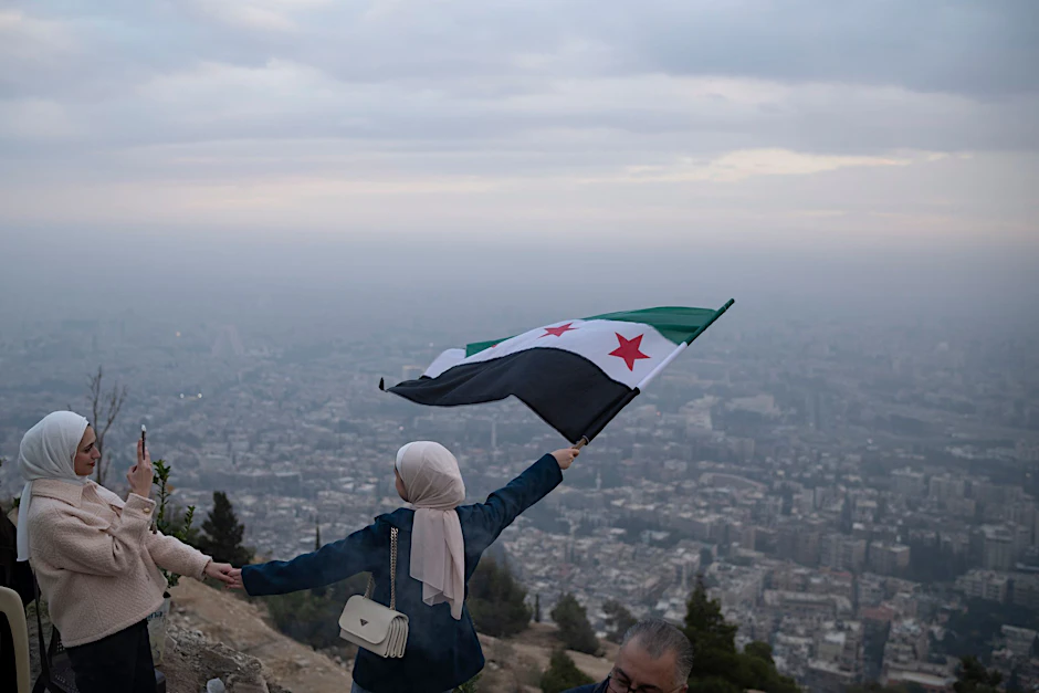 Dezember 2024: Eine junge Frau posiert für ein Foto mit einer Flagge der syrischen Opposition an einem Aussichtspunkt auf dem Berg Qasiyun oberhalb der Stadt Damaskus.