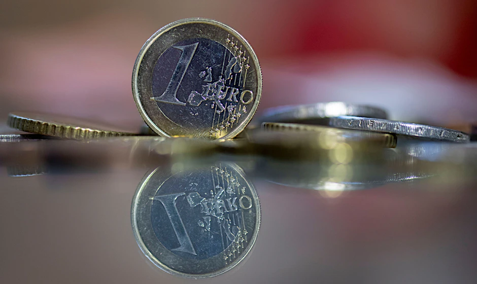 Eine 1-Euro-Münze steht auf einem Tisch, umgeben von anderen Euro-Münzen.