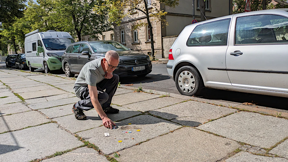 Hans Greiner untersucht ein Einschussloch auf einer Gehwegplatte.