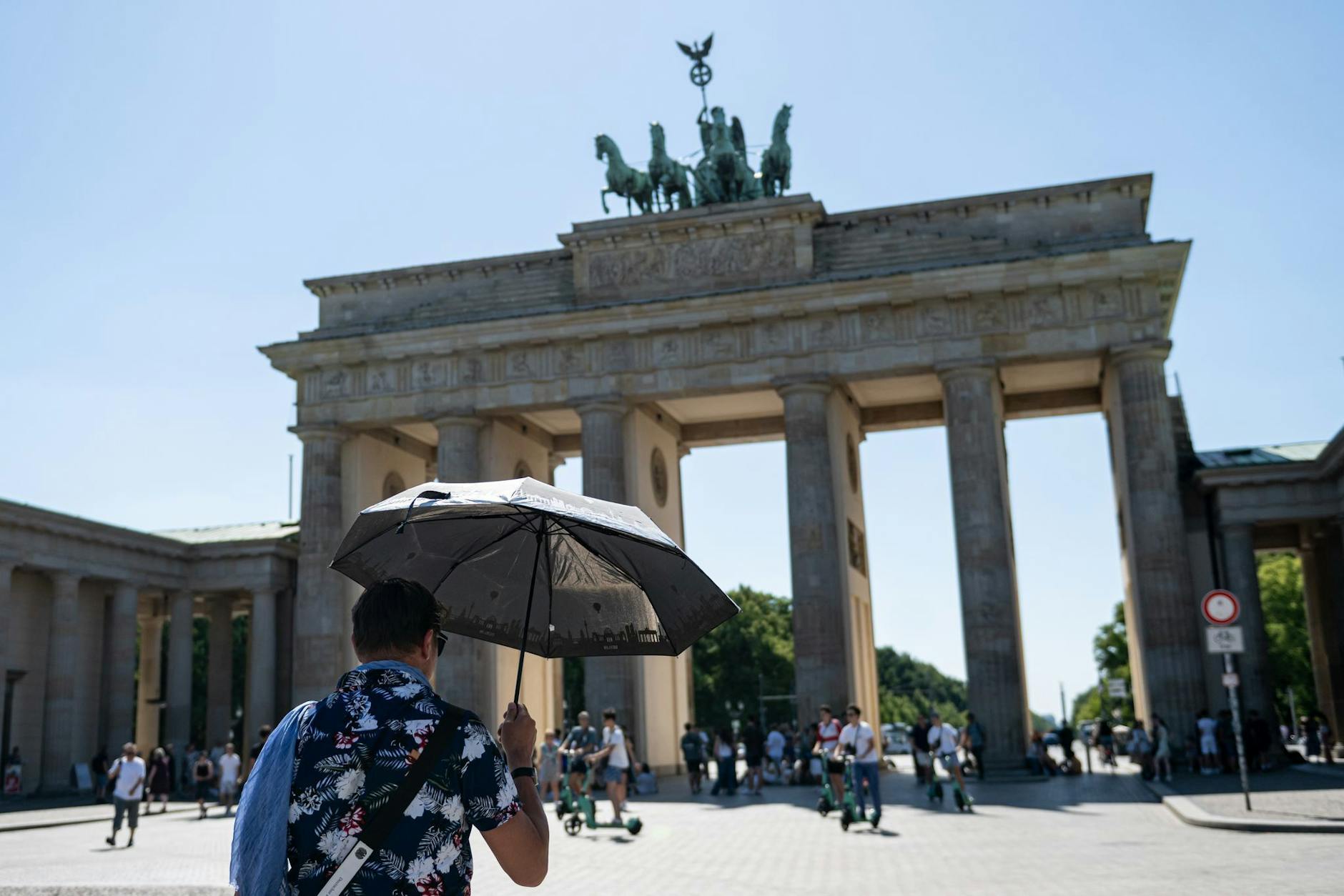 Eine Person läuft mit Schirm als Sonnenschutz bei hohen Temperaturen über den Pariser Platz.