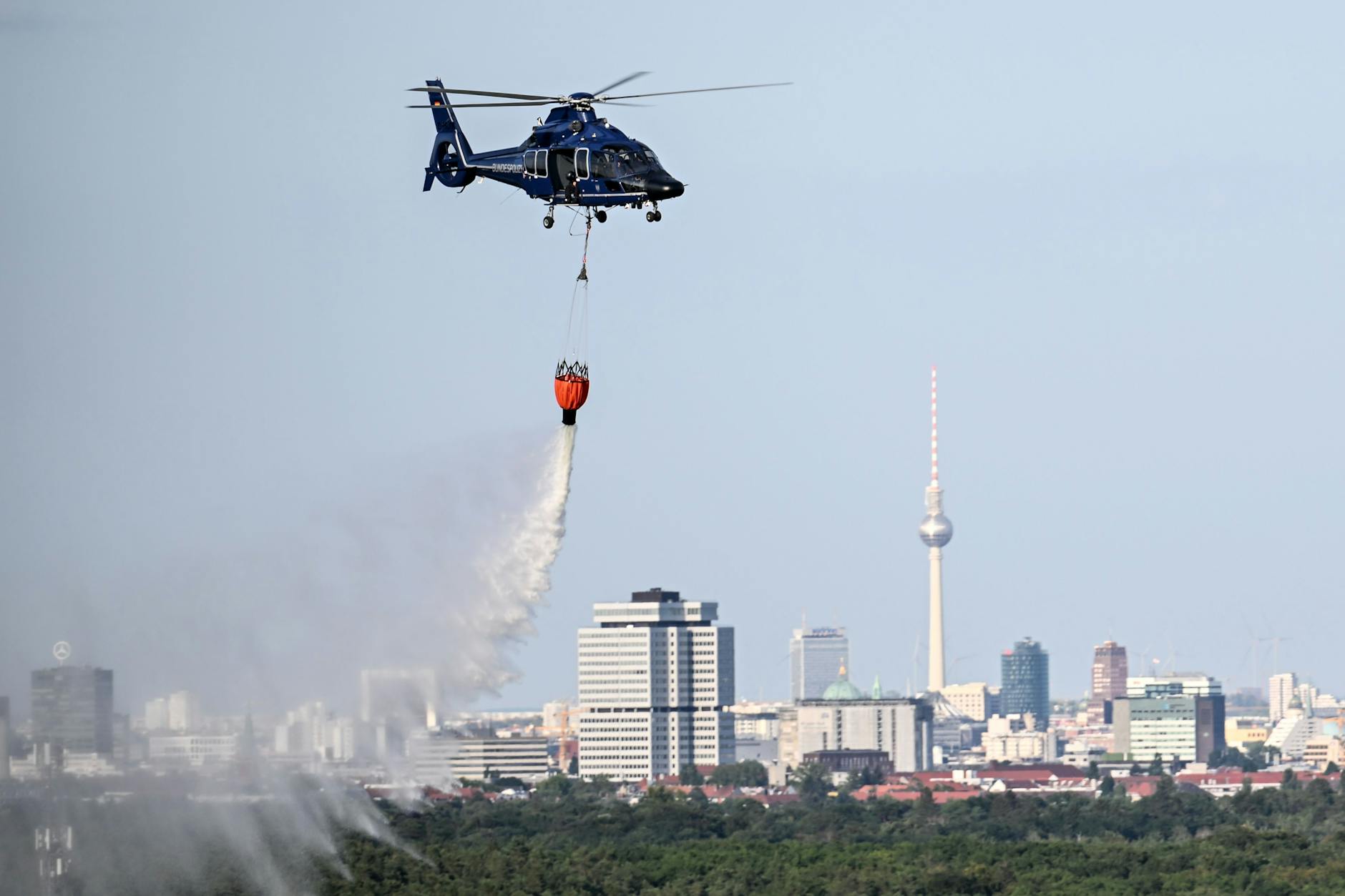 Ein Hubschrauber der Bundespolizei wirft Wasser über der Brandstelle im Grunewald ab.