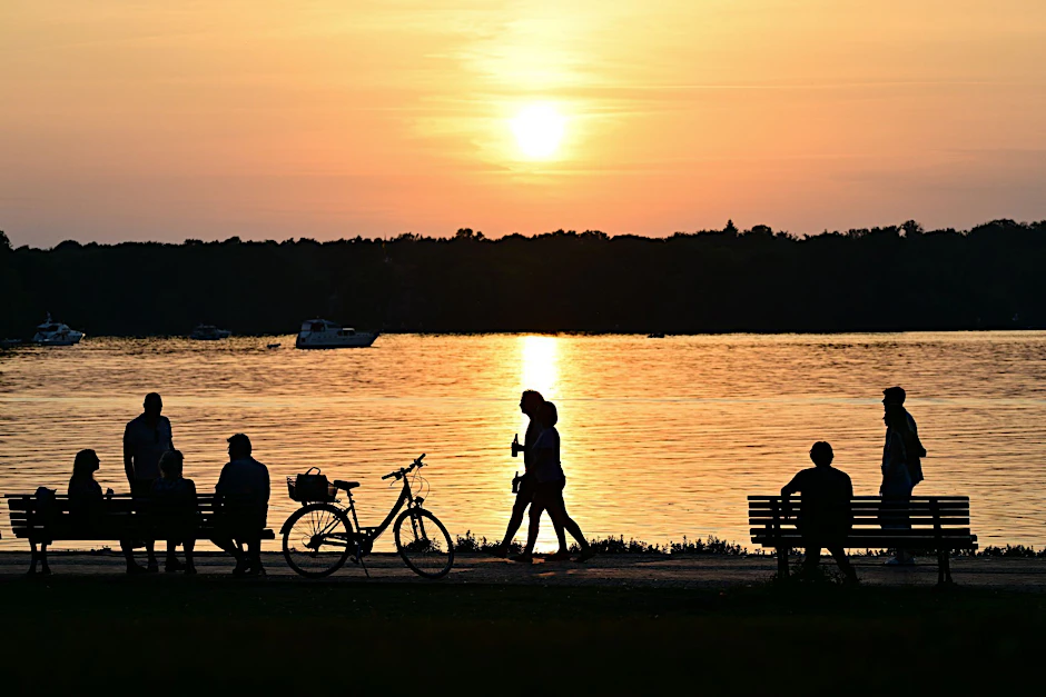 Menschen gehen bei Sonnenuntergang am Ufer des Tegeler Sees. (zu dpa: «Bilder des Tages»)