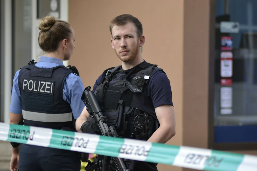 Ein Polizist steht mit einem Maschinengewehr am Tatort und sichert den Bereich.