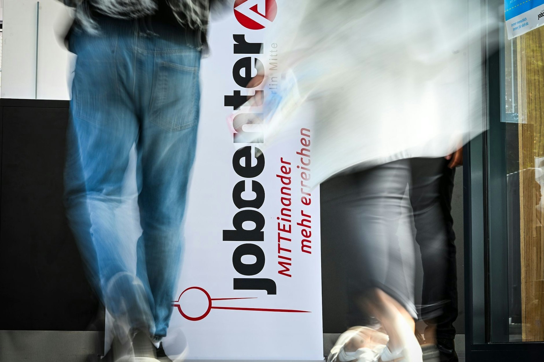 Personen gehen auf der Jobmesse am Logo des Jobcenters Berlin-Mitte vorbei. (Symbolbild)