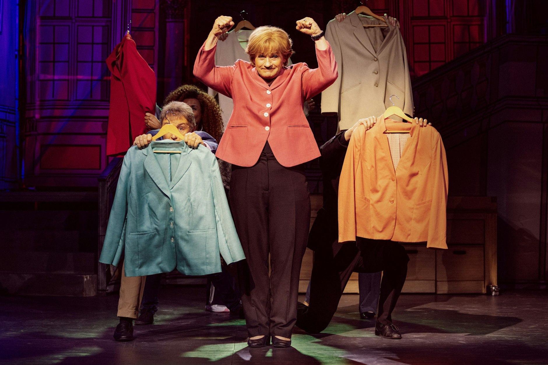 Mitte: Christoph Marti als Miss Merkel umgeben von Blazern und Ensemble