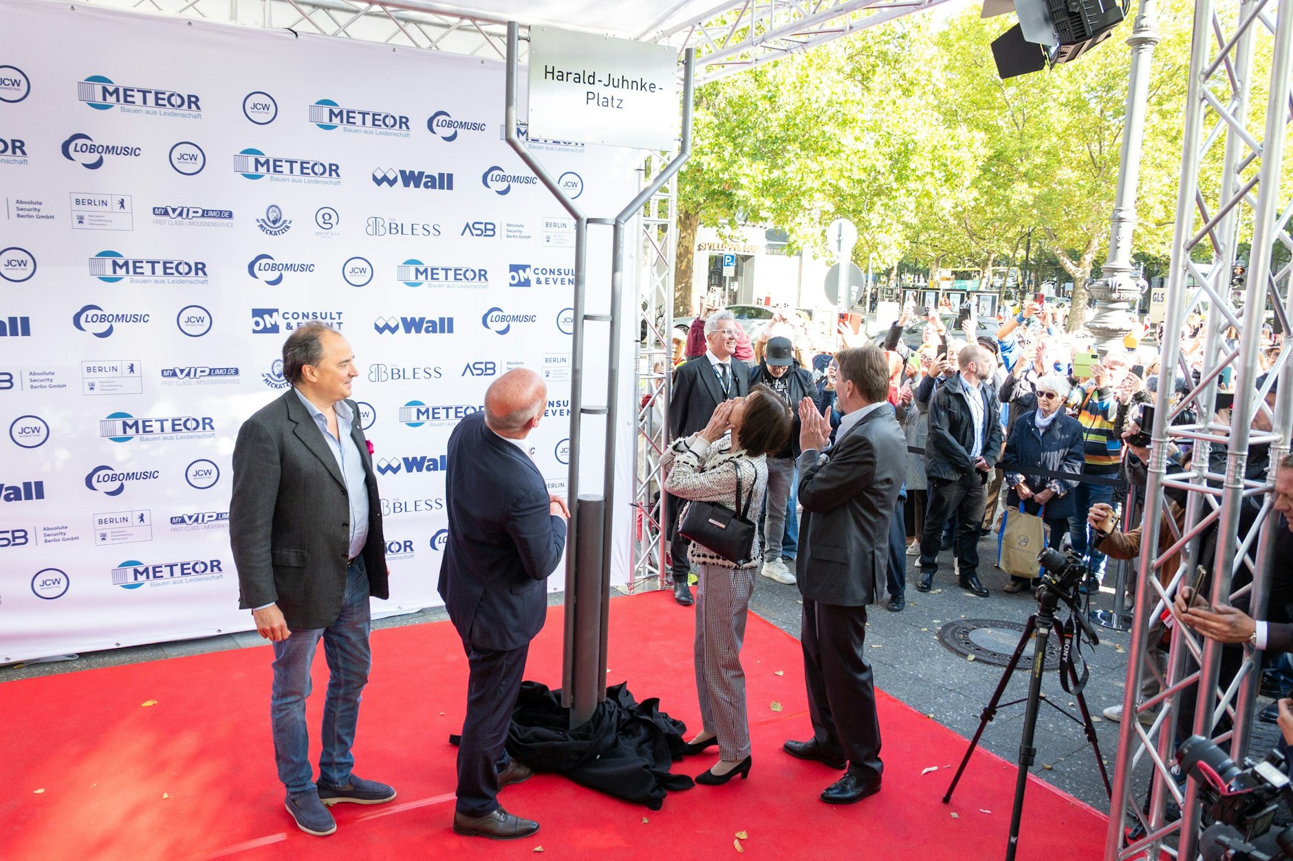 Festlich eingeweiht: Vort dem Schild vom Harald-Juhnke-Platz in Berlin stehen Juhnke-Sohn Oliver, der Regierende Kai Wegner, Susanne Juhnke und Juhnkes Ex-Manager Peter Wolf.