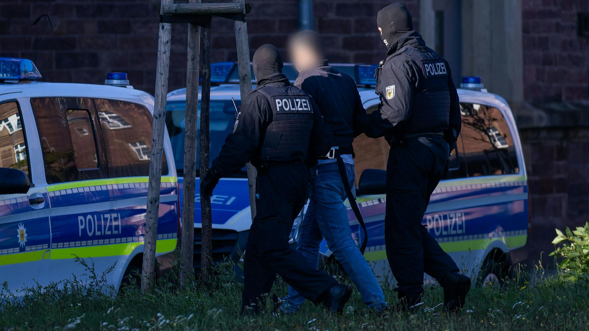 Einer der drei Festgenommenen wird von zwei Bundespolizisten zu den Einsatzfahrzeugen geführt.
