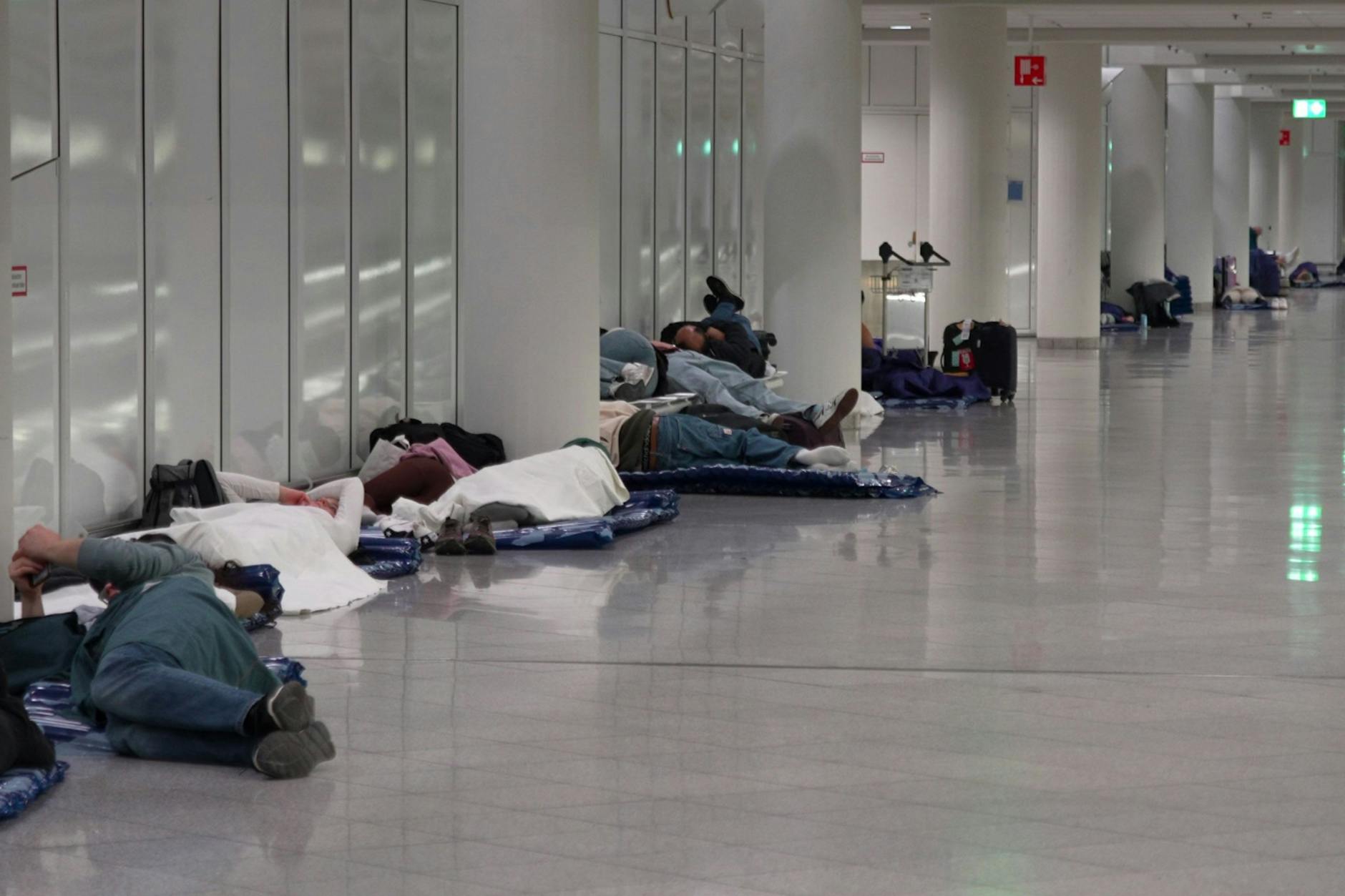 Menschen ruhen sich nach möglichen Drohnensichtungen am Flughafen München aus. Der Flughafen München hat am Abend wegen möglicher neuer Drohnen-Sichtungen wieder den Betrieb eingestellt.