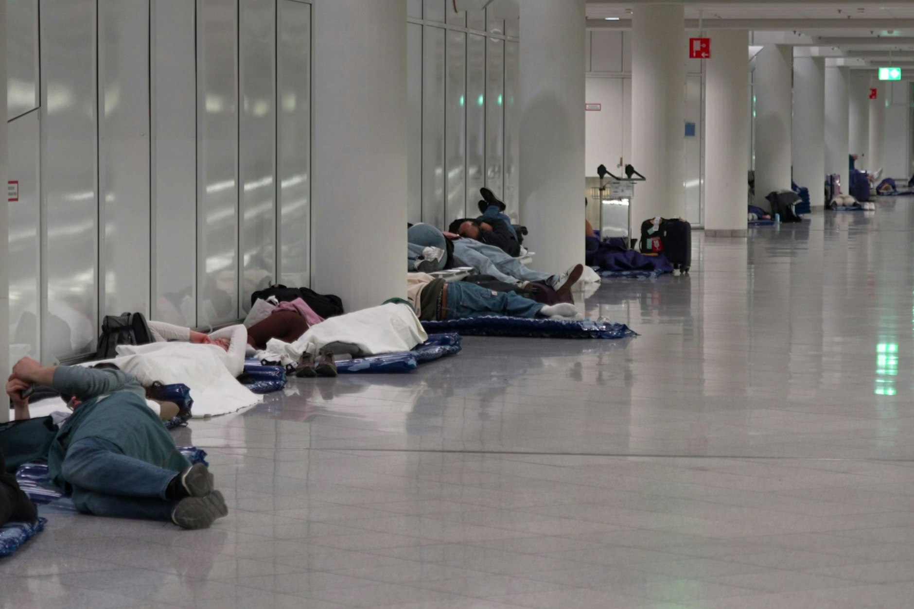 Menschen ruhen sich nach möglichen Drohnensichtungen am Flughafen München aus. Der Flughafen München hat am Abend wegen möglicher neuer Drohnen-Sichtungen wieder den Betrieb eingestellt.