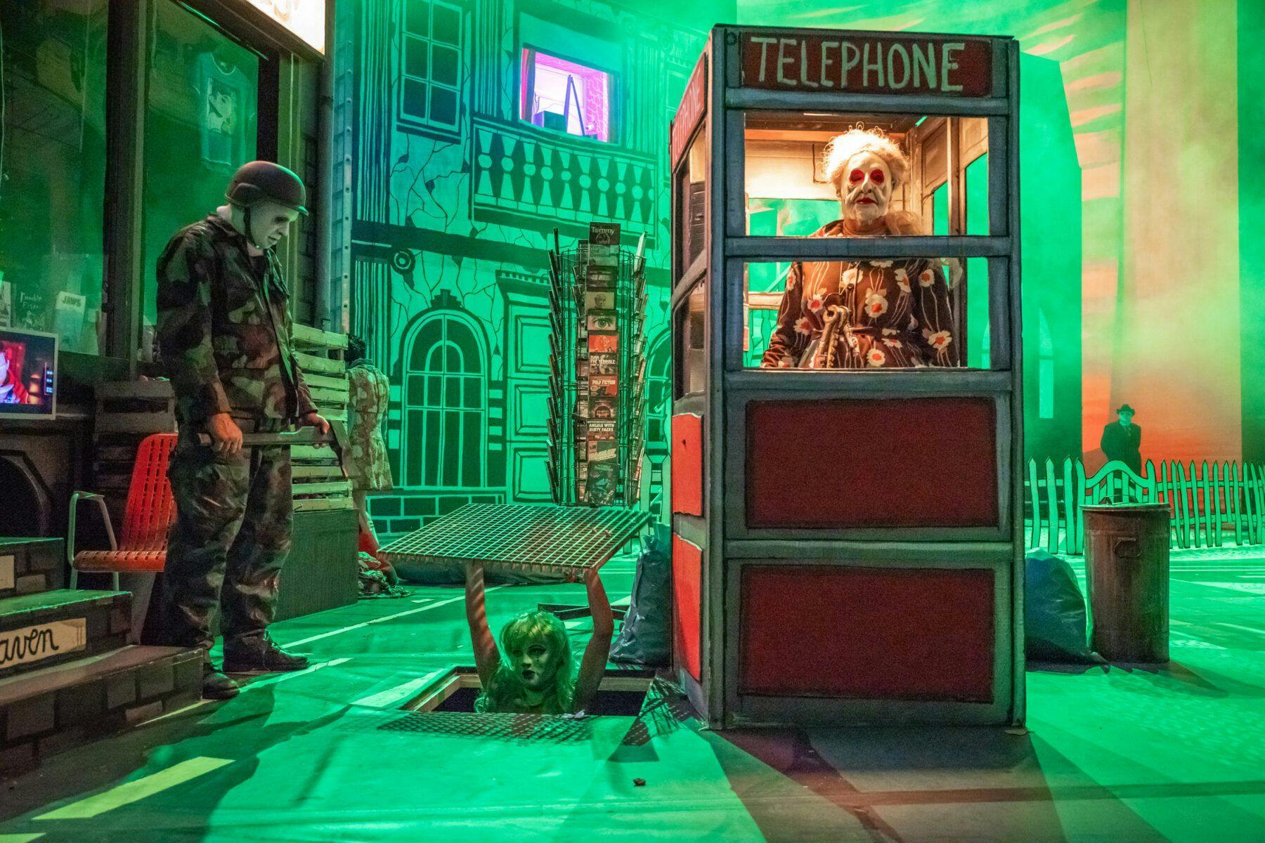 Die Mutter in der Telefonzelle, die grüne Frau steigt aus der Kanalisation, die Axt wartet auf ihren Einsatz. Szene aus „Peer Gynt“