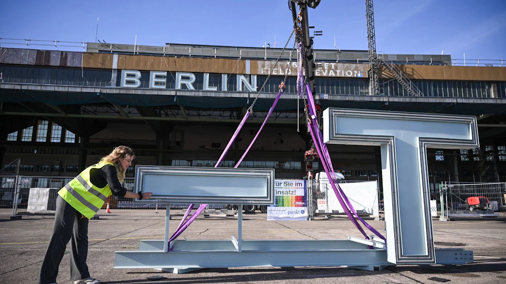 Die Restauratorin Sarah Gschlecht erklärt bei der Wiederanbringung des Schriftzugs „Berlin-Tempelhof“ auf dem Dach des ehemaligen Flughafens Tempelhof die Restauration.