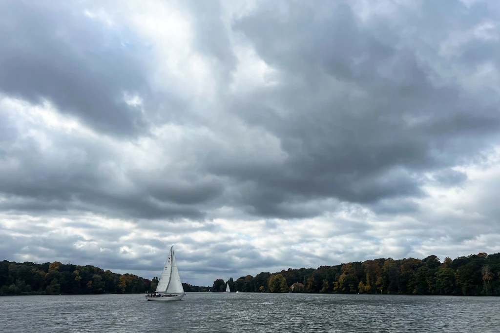 Ein Segelboot segelt auf der Havel an der Pfaueninsel vorbei. Die Wolken hängen schon tief.