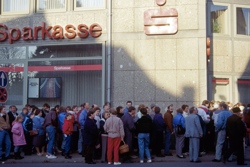 Menschen stehen zur Auszahlung des Begrüßungsgeldes vor einer Sparkasse.