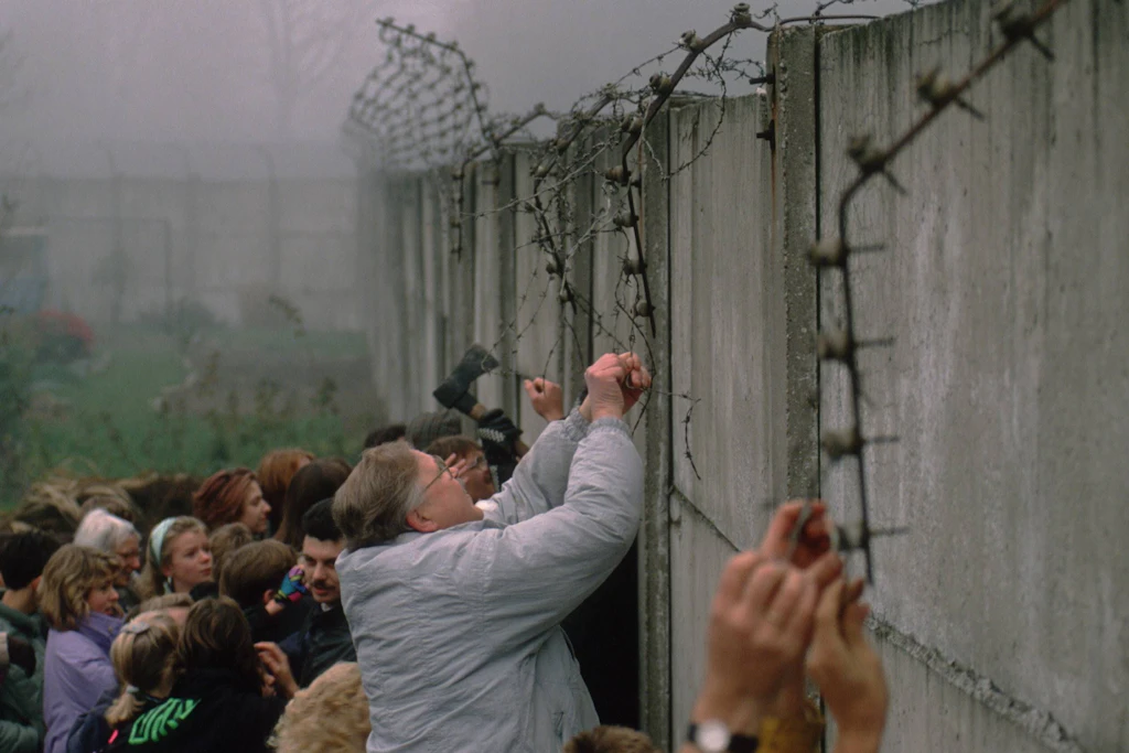 Menschen reißen Stacheldraht von der Berliner Mauer.