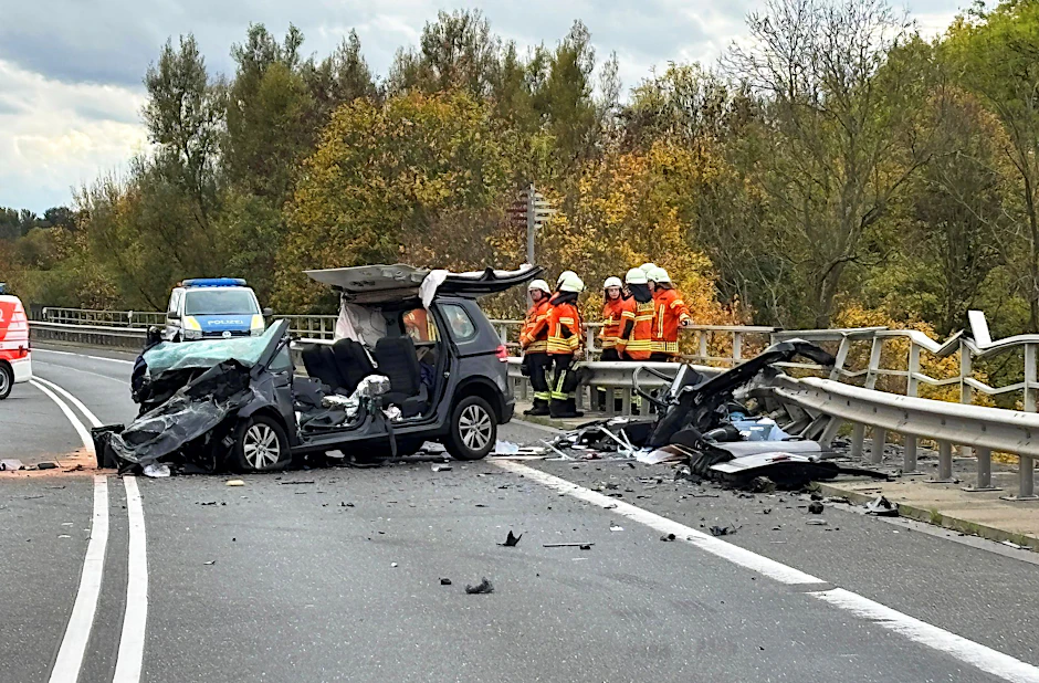 Einsatzkräfte der Feuerwehr stehen an der Unfallstelle. Das Unfallauto ist nur noch ein Wrack.