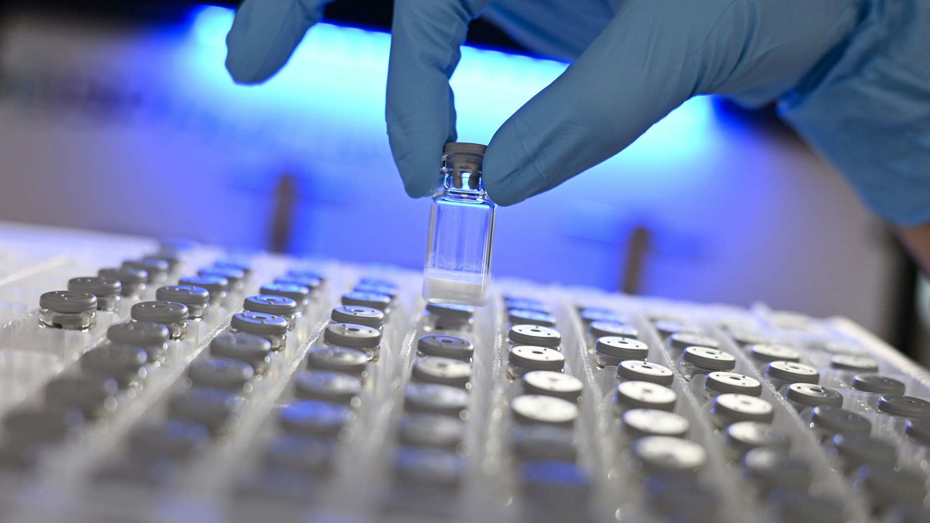 Eine Laborantin entnimmt in einem Labor des Pharma- und Technologiekonzerns Merck eine gefriergetrocknete Probe aus einem Behälter.