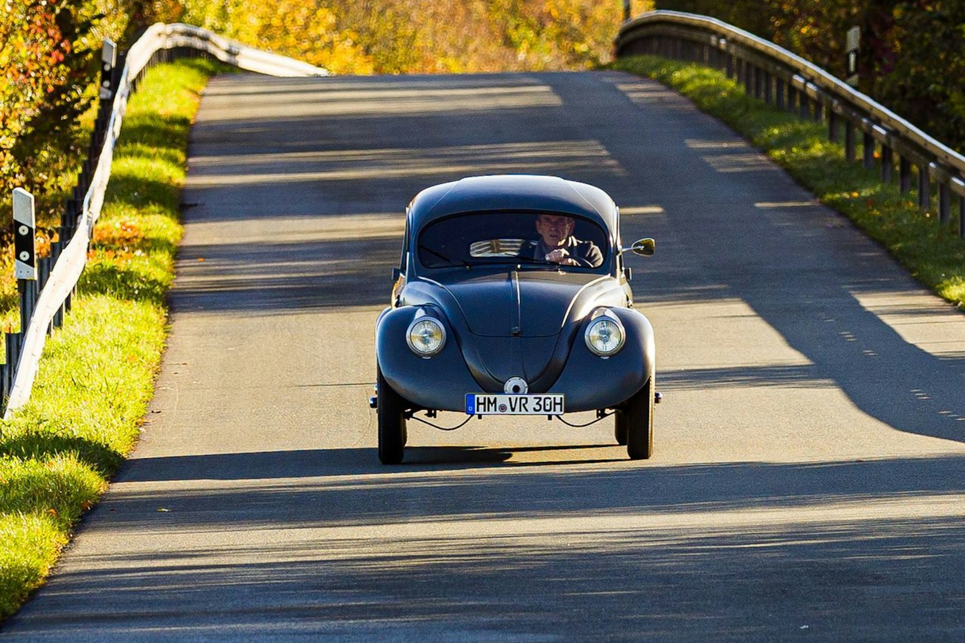 Traugott Grundmann mit seinem VW Käfer auf der Landstraße. Um durch die Frontscheibe schauen zu können, muss er sich ducken.