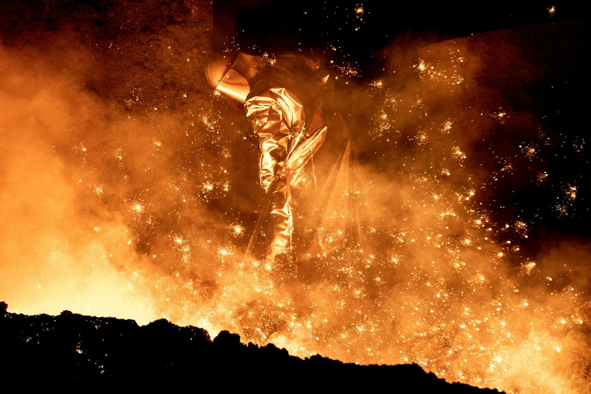 Ein Mitarbeiter reinigt in einem Stahlwerk die Abstichrinne am Hochofen.