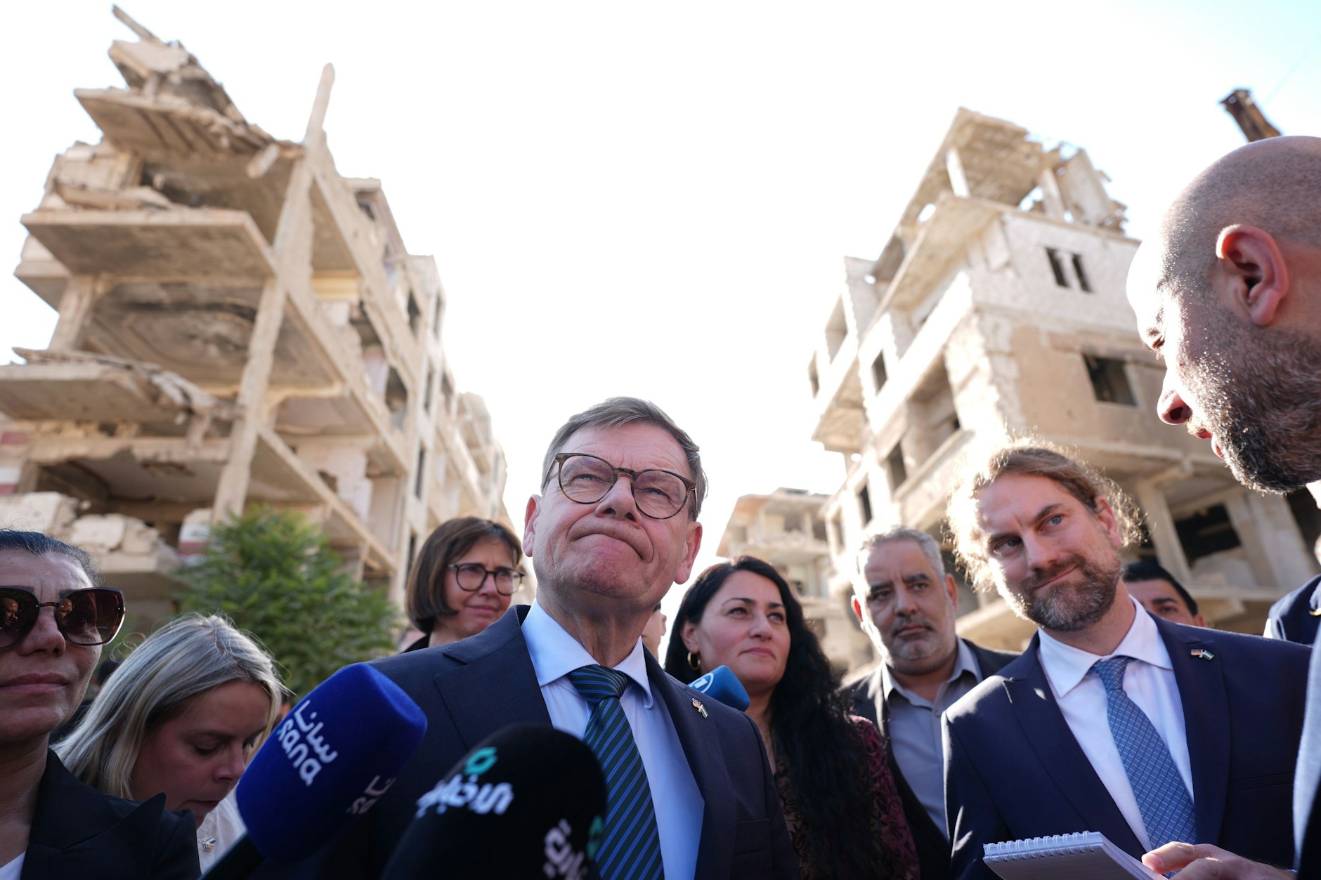 Johann Wadephul (CDU, M.), Bundesminister des Auswärtigen, steht während seines Besuchs eines humanitären Projekts mit Raed al-Saleh (r.), Minister für Katastrophenschutz in Syrien, in einer Straße vor im Bürgerkrieg zerstörten Häusern.