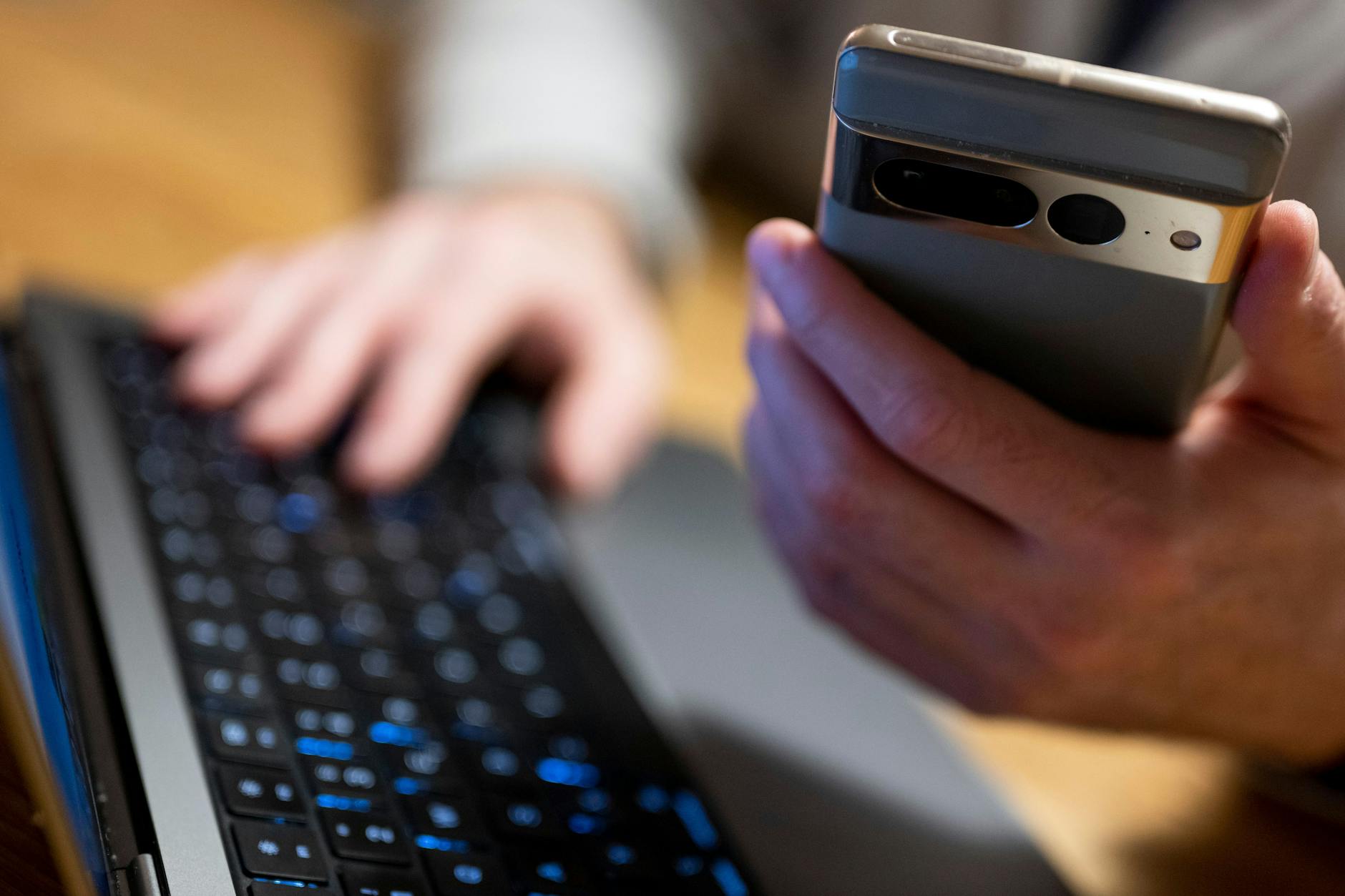 Ein Mann sitzt am Laptop und hält ein Smartphone mit in der Hand.