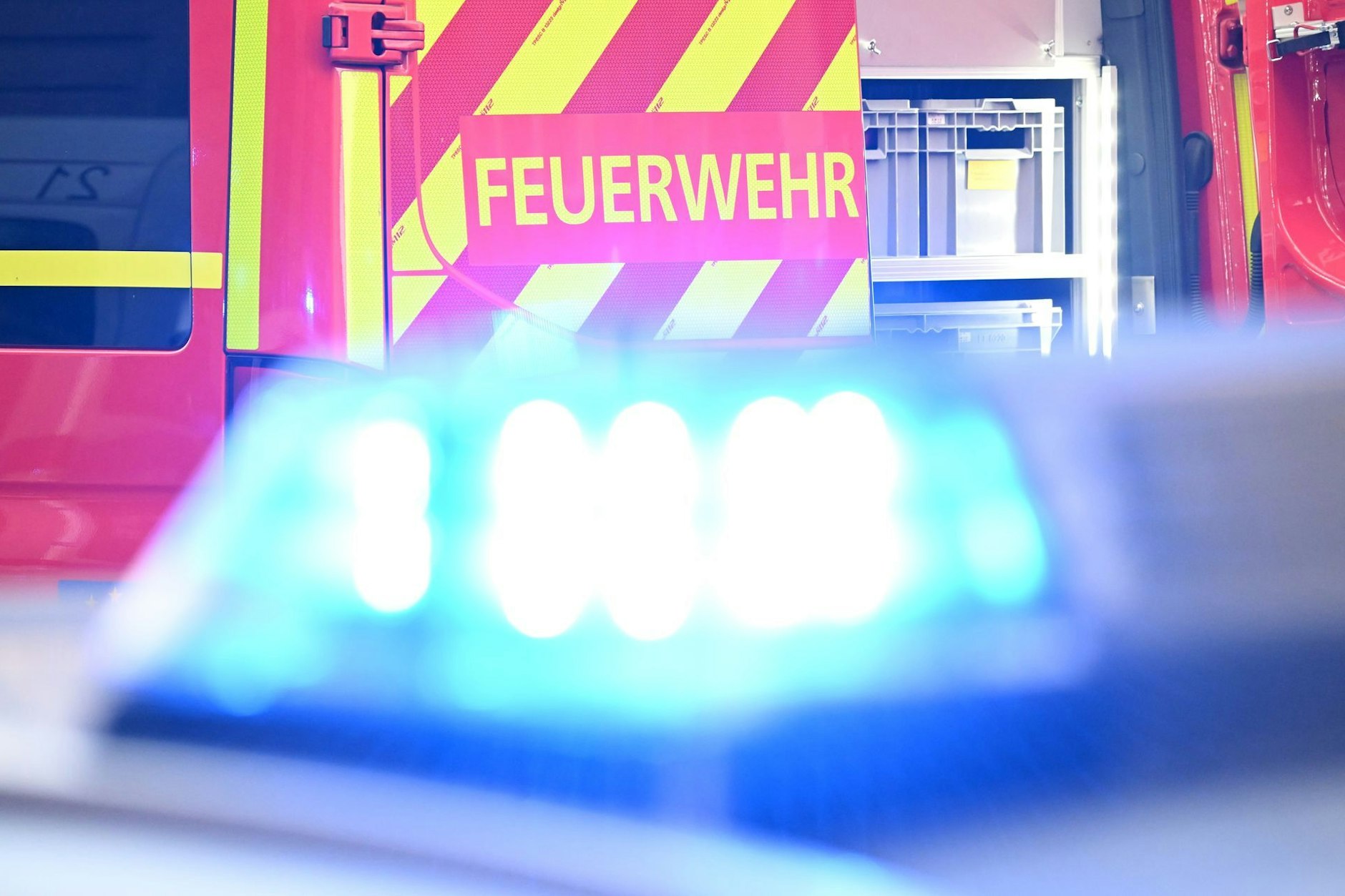 Ein Fahrzeug der Feuerwehr steht bei einem Einsatz auf einer Straße, während im Vordergrund das Blaulicht eines Polizeifahrzeugs zu sehen ist. (zu dpa: «13 Menschen bei Brand in Wriezen verletzt»)