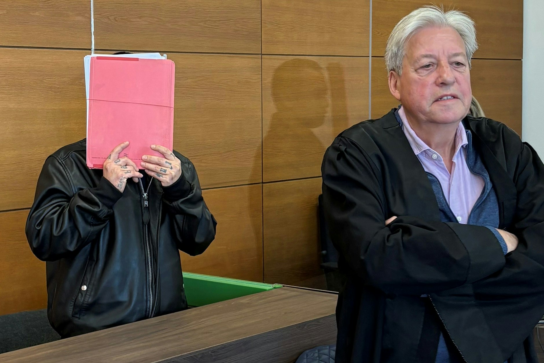 Der Angeklagte verbirgt im Macheten-Prozess sein Gesicht mit einem Aktendeckel.