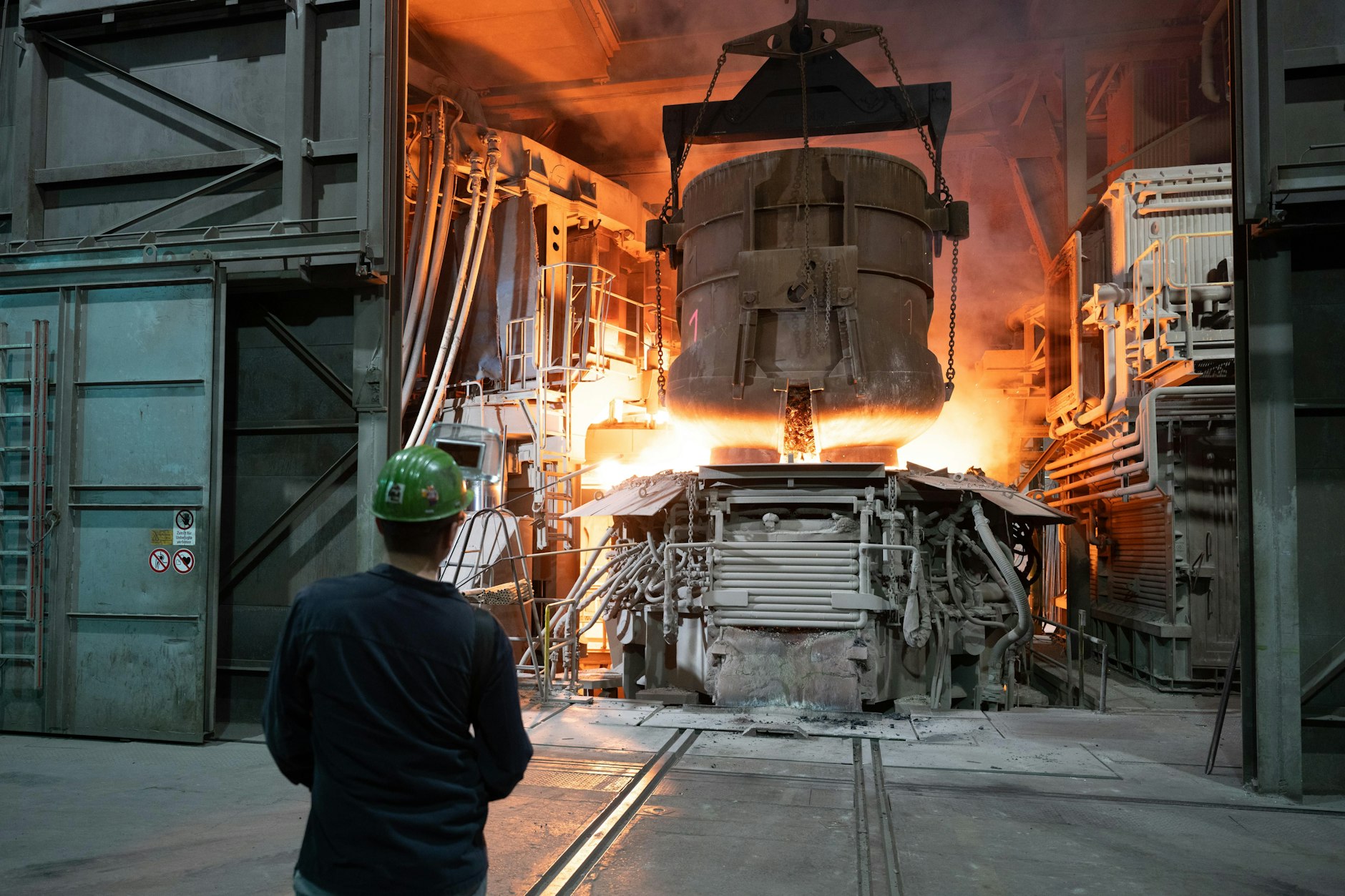 Ein Mitarbeiter steht in einer Werkhalle der BGH Edelstahl Freital GmbH hinter einem Schrottkorb an einem Lichtbogenofen. 