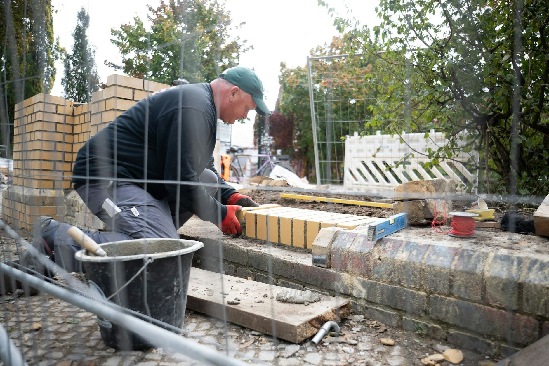Ein Handwerker mauert am Eingang zum Görlitzer Park an der Lübbener Straße eine neue Mauer auf, die dann neben einem Metalltor stehen wird.