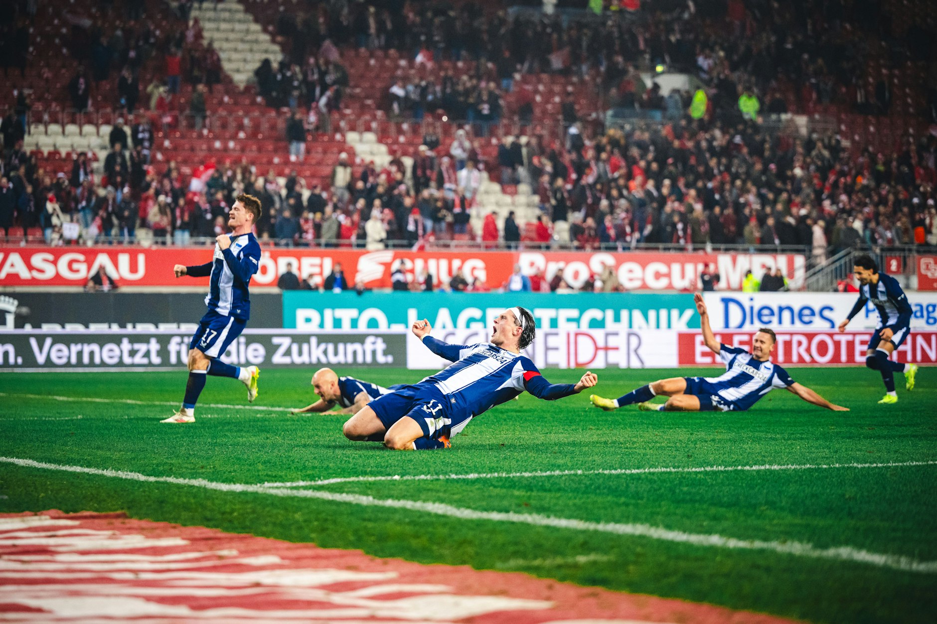 Toni Leistner, Sebastian Grönning, Fabian Reese und Paul Seguin (v.l.) rutschen vor Freude nach dem Sieg über den Rasen Richtung der 5000 mitgereisten Hertha-Fans.
