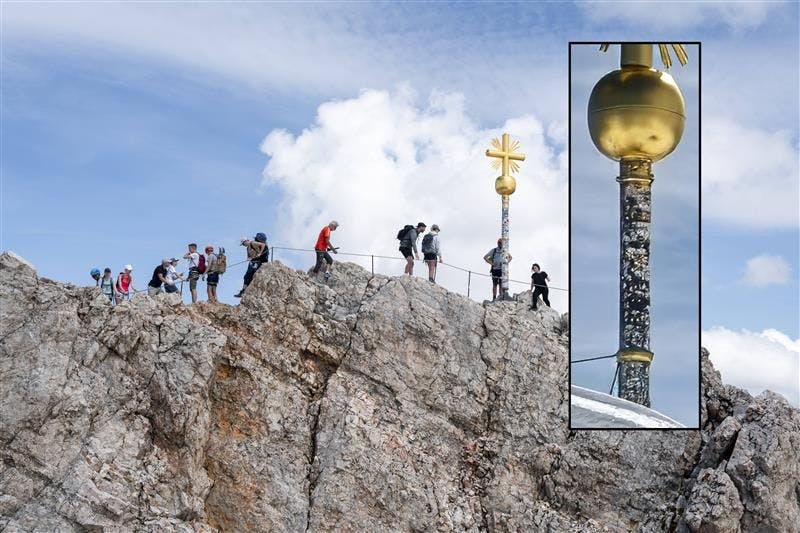 Die Nahaufnahme zeigt, wie das goldene Gipfelkreuz auf der Zugspitze mit Stickern beklebt ist. Bis hin zur Kugel.