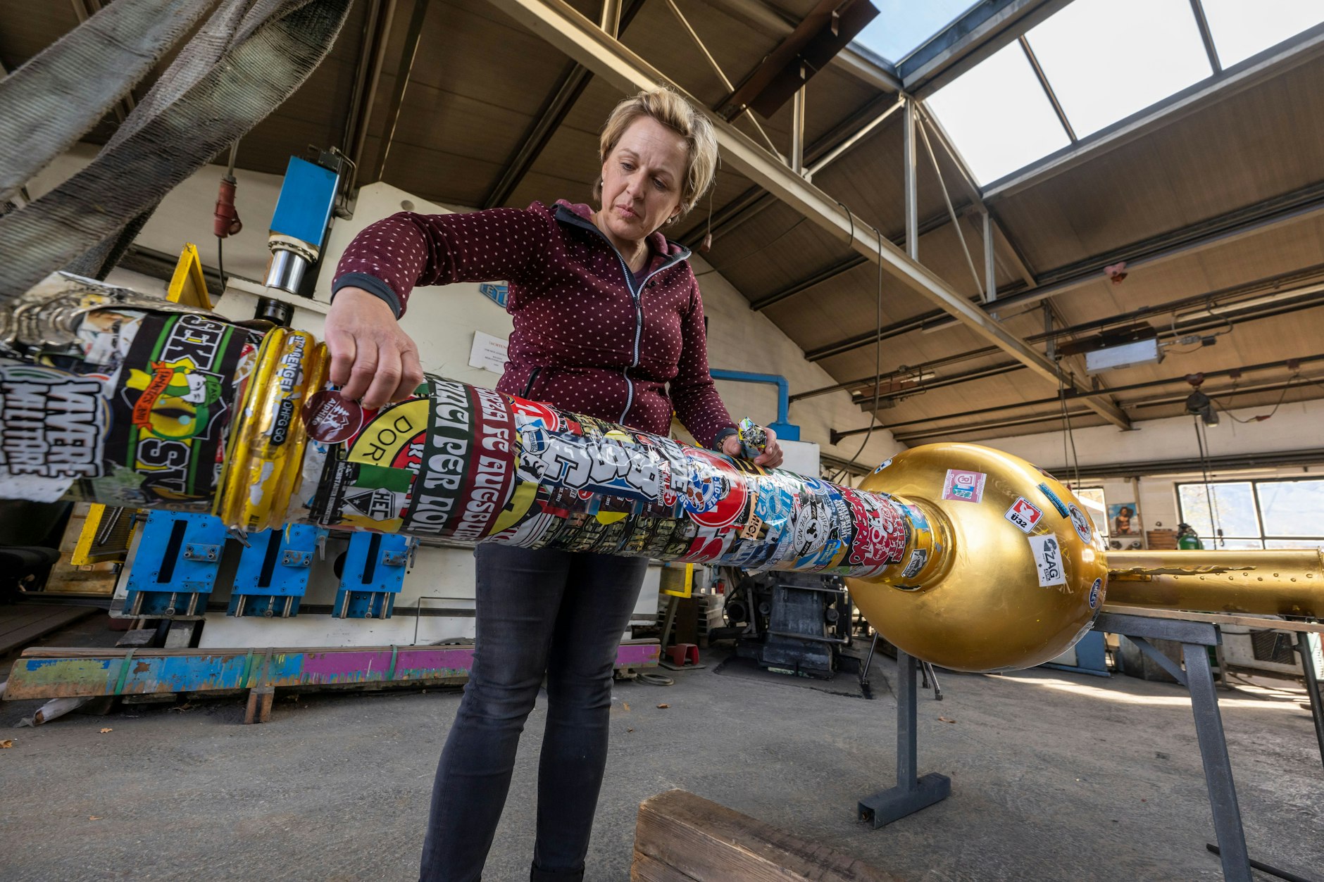 Andrea Würzinger entfernt Aufkleber vom Zugspitz-Gipfelkreuz, das anschließend in ihrem Kunstschmiede-Betrieb restauriert wird.