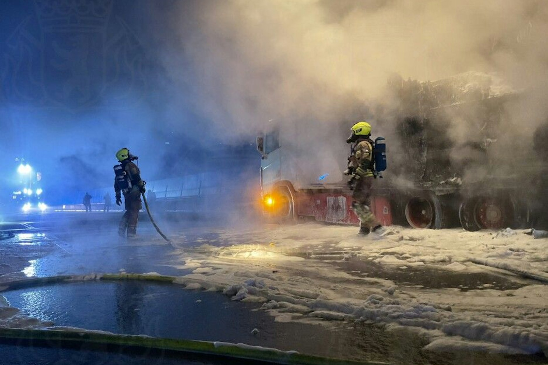 A113: Feuerwehrleute stehen neben dem ausgebrannten Brummi.