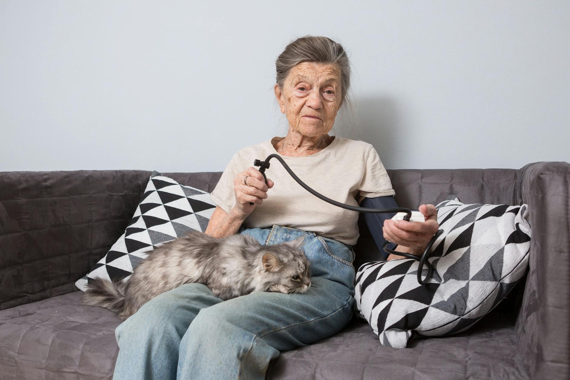 Eine hochbetagte Frau sitzt auf dem Sofa und misst ihren Blutdruck.