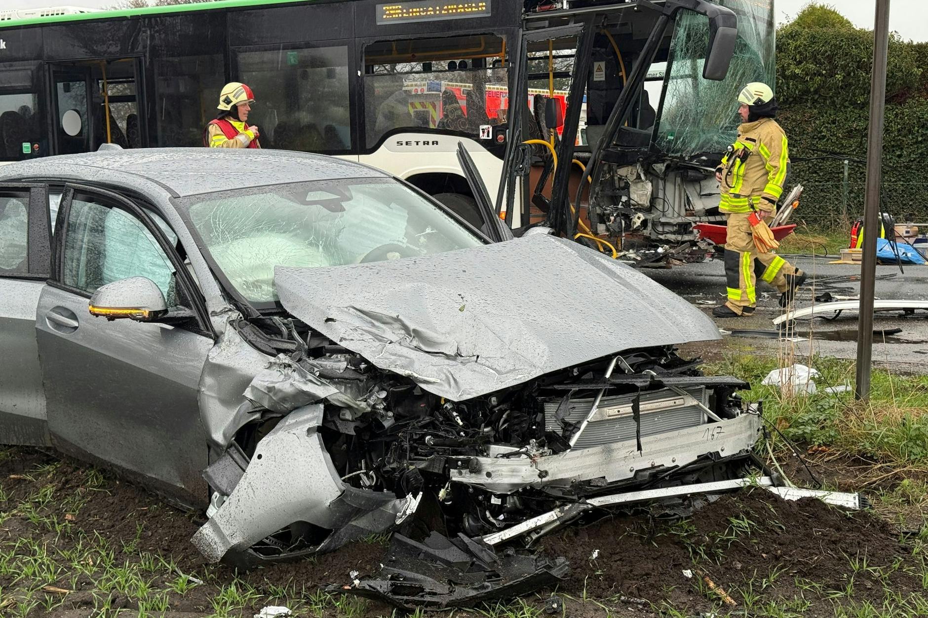 Ein Bus und ein Auto stehen nach Unfall demoliert an einer Straße.