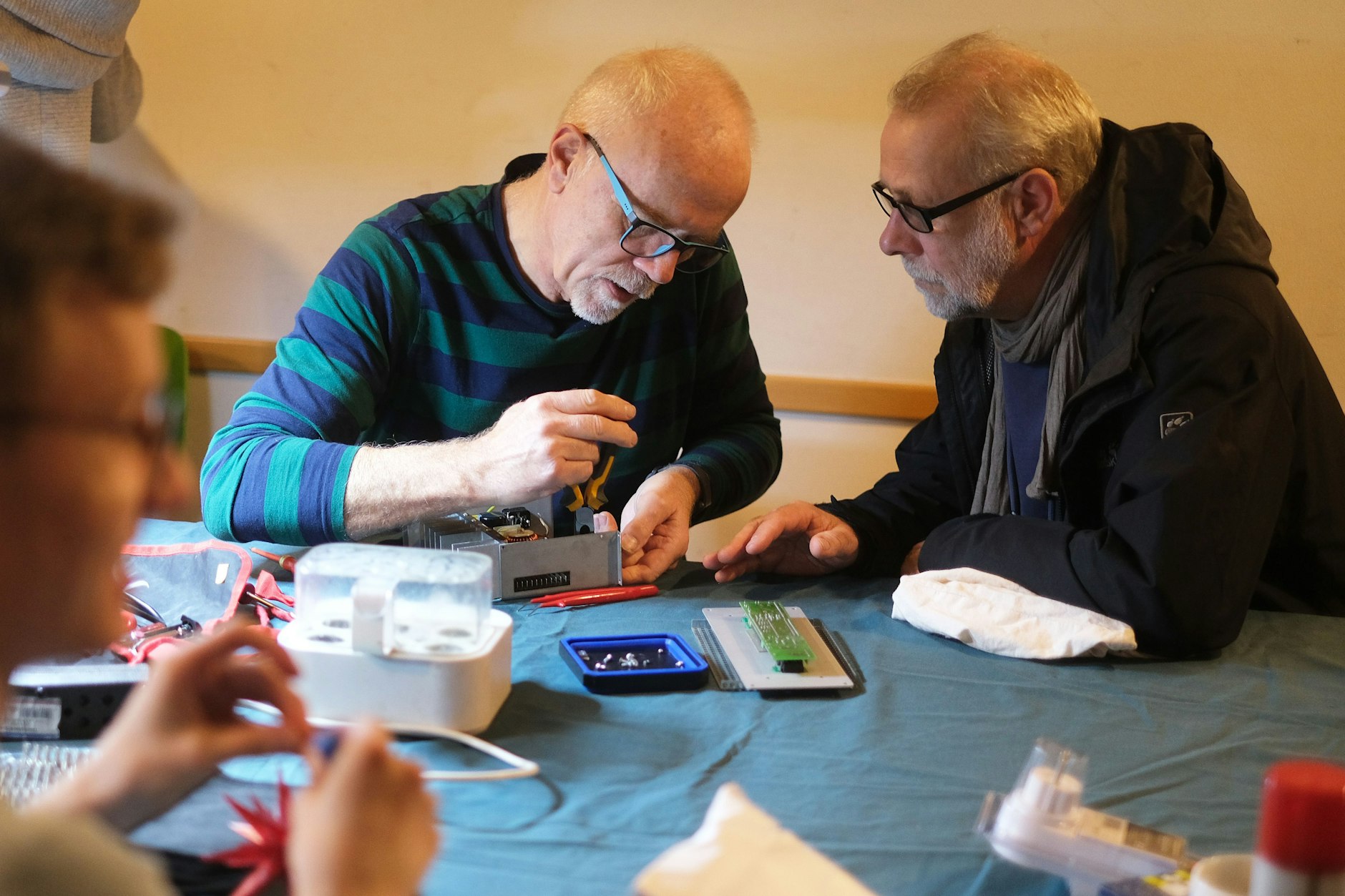 Medizintechniker Hajo Jürgens (links) hat sich eines defekten Stromumwandlers eines Besuchers des Repair-Cafés angenommen. Vor ihm wartet ein Eierkocher auf Reparatur.